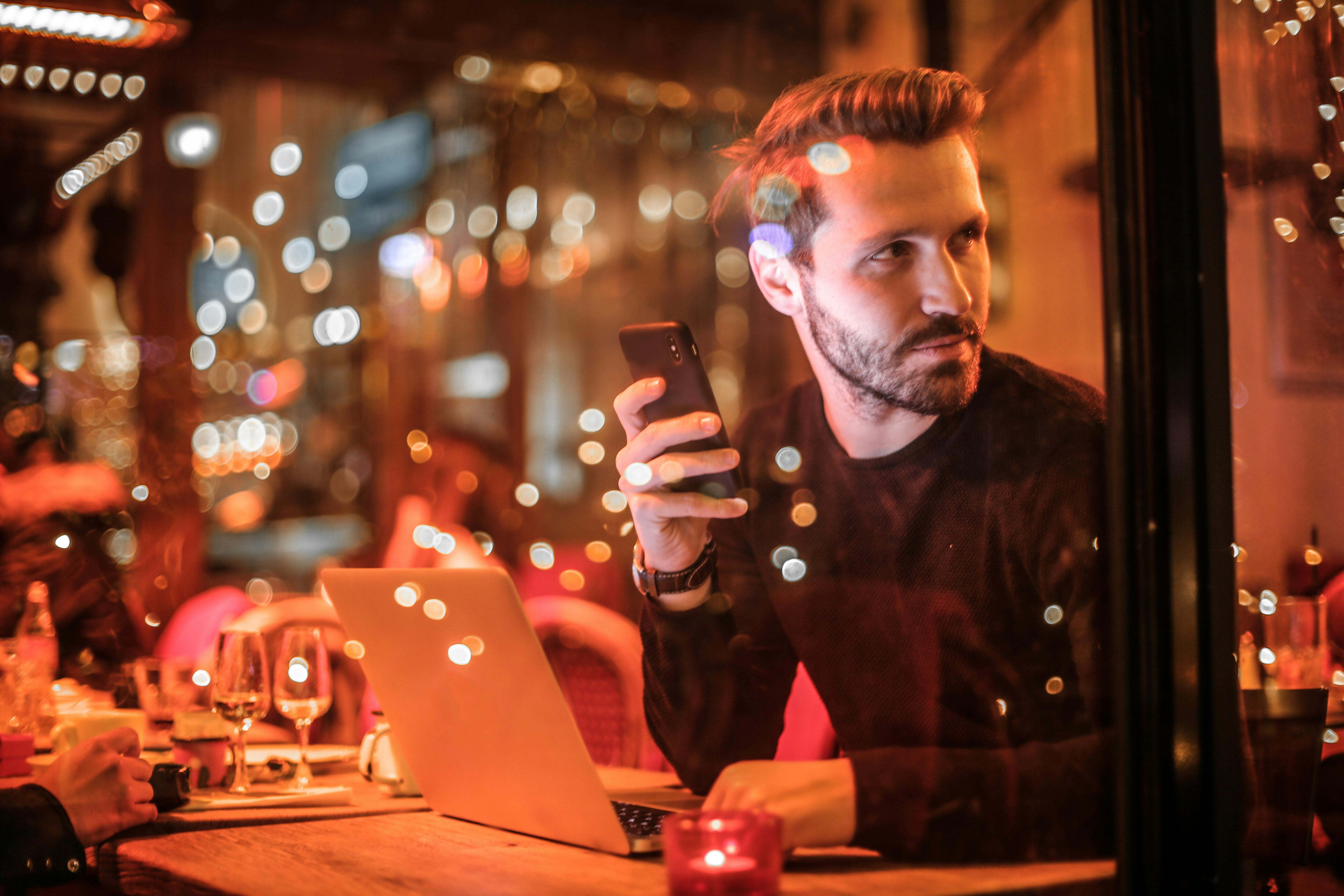 A man sitting in a cafe with his phone and laptop.