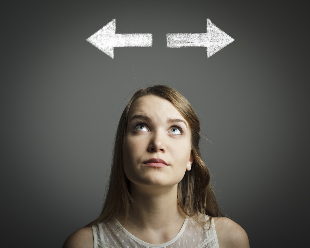 Woman standing under two arrows pointing in opposide directions.