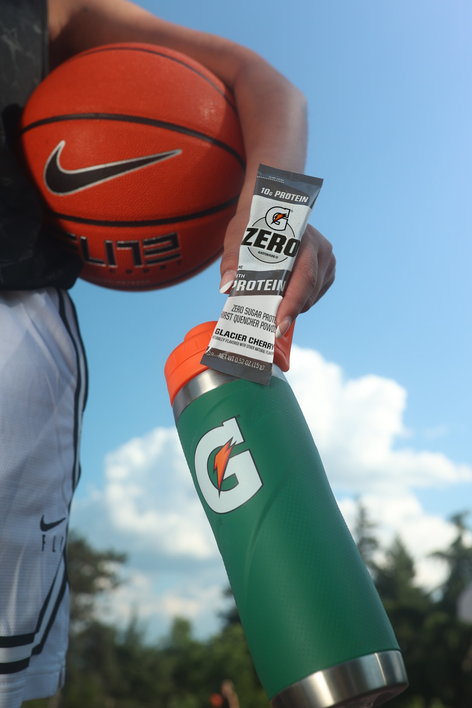 G Zero with Protein held next to a basketball and Gx Stainless Steel bottle