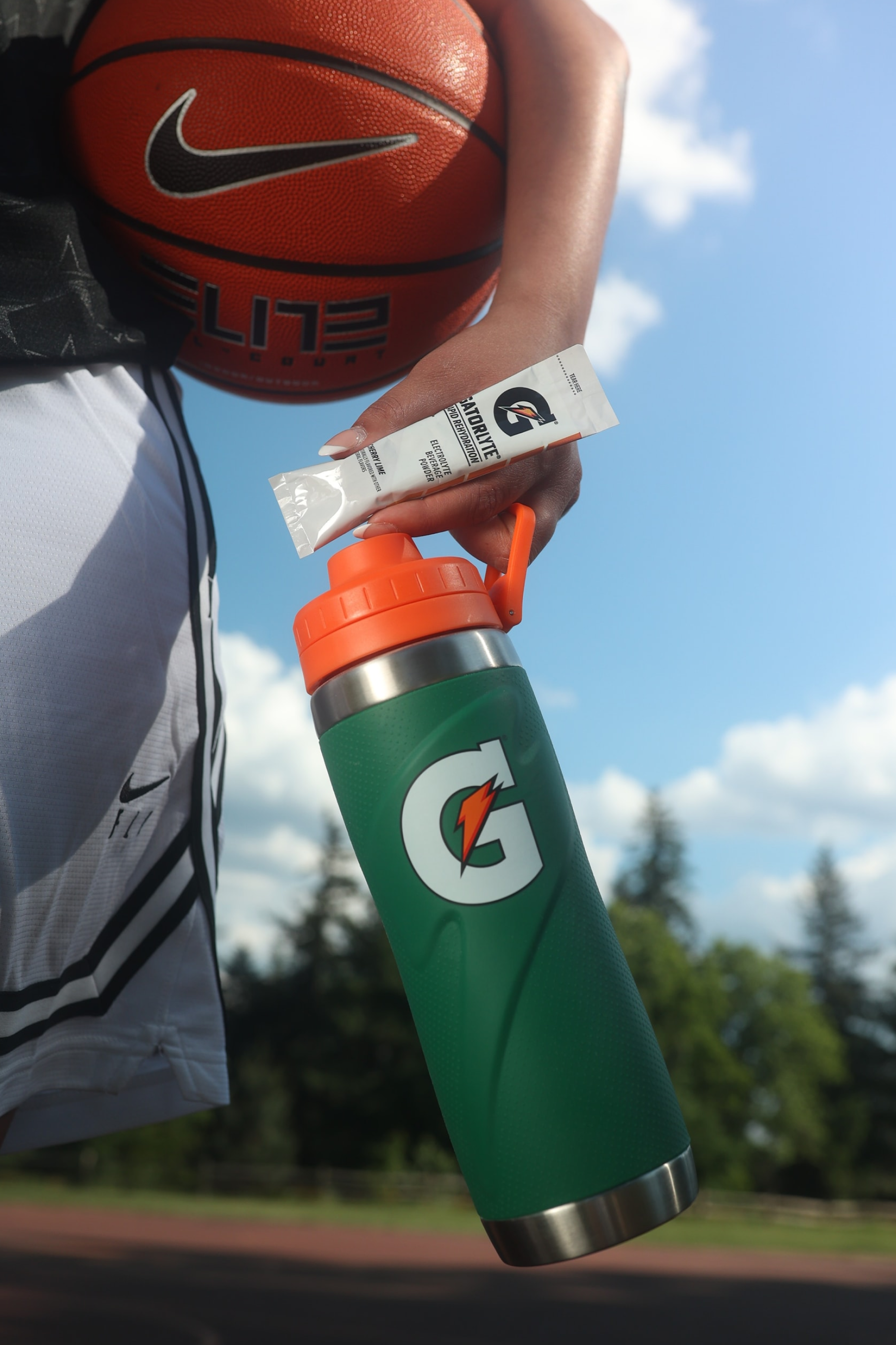 Athlete holding gatorlyte single serve powder in cherry lime with Gx stainless steel bottle