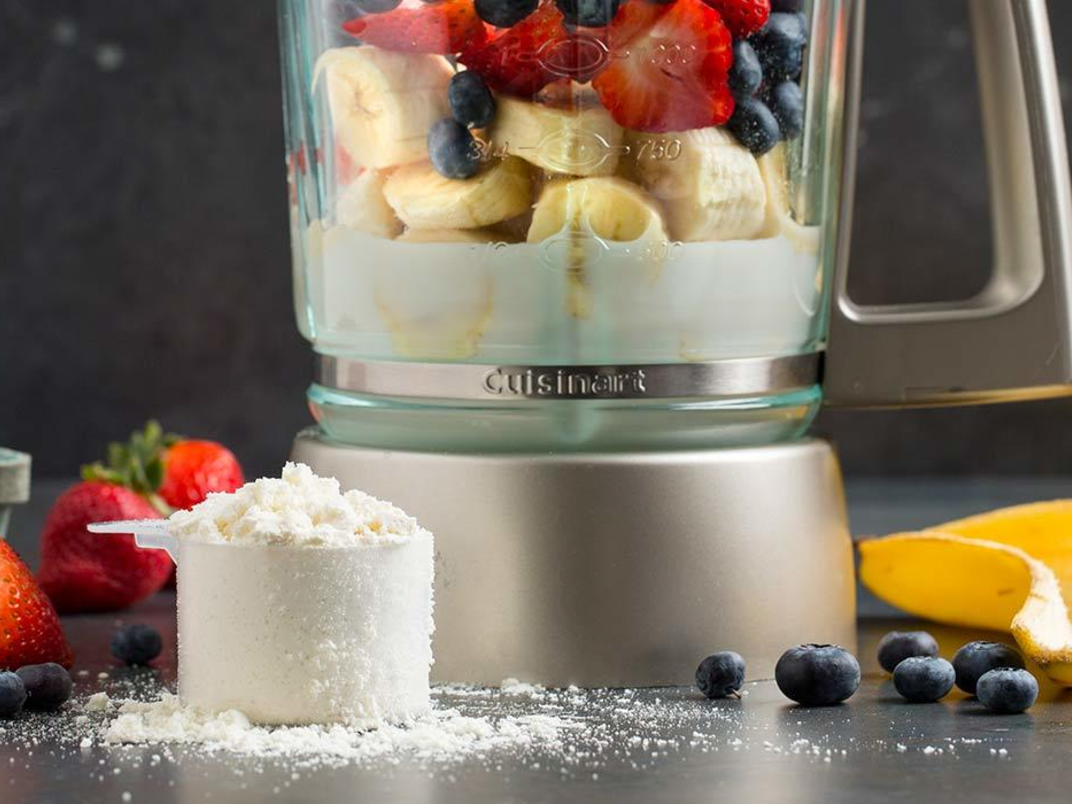 Protein powder next to a blender with fruit