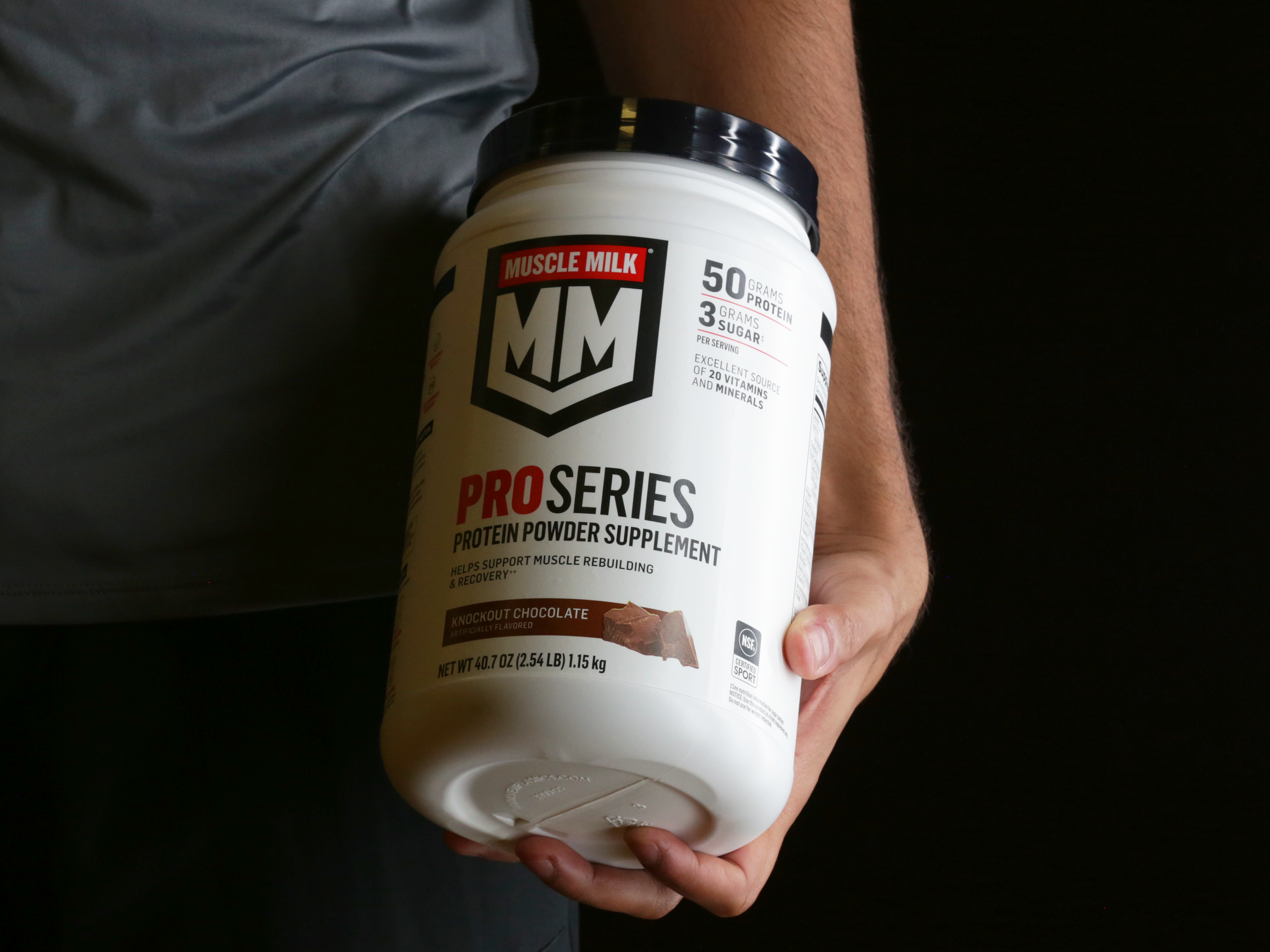 Athlete holding Muscle Milk Pro Series Knockout Chocolate Protein Powder canister