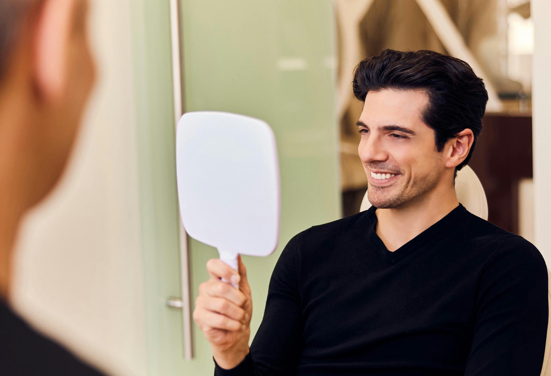 Man looking at himself in a handheld mirror smiling