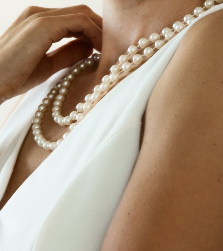 Woman's neck area while wearing a white top and pearl necklaces