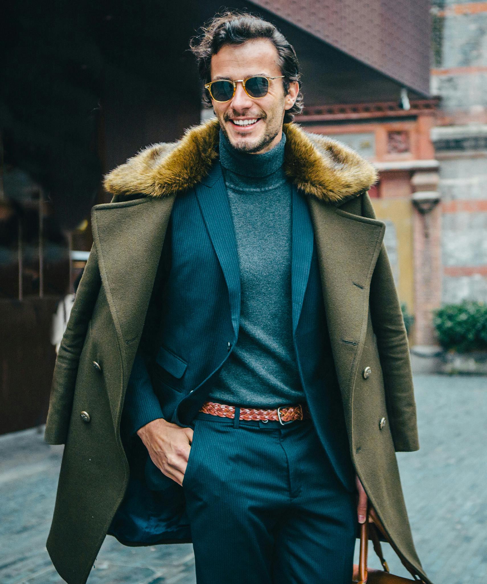 man in a coat and sunglasses is smiling while holding a bag