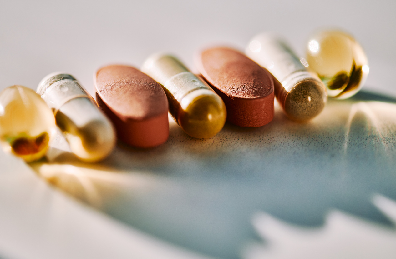 Close-up of assorted vitamin and supplement capsules on a reflective surface.