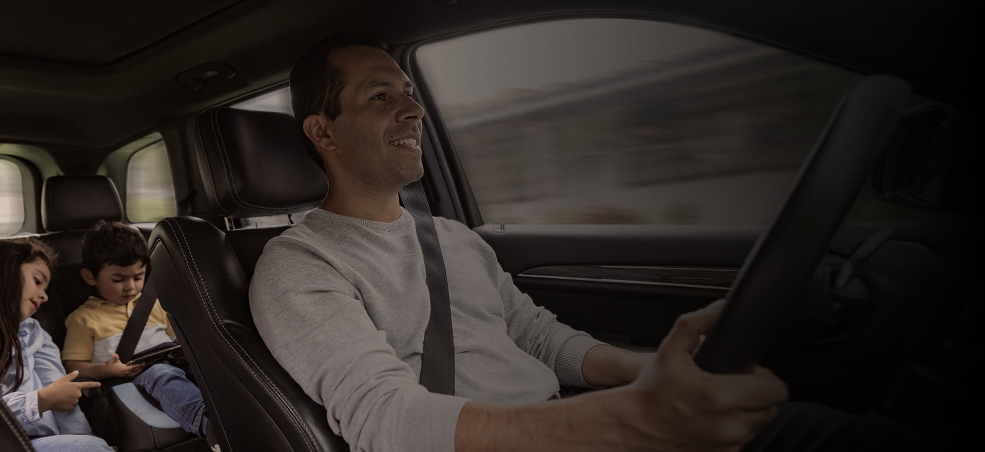 a father is driving while his two children are looking at a laptop in the back seats