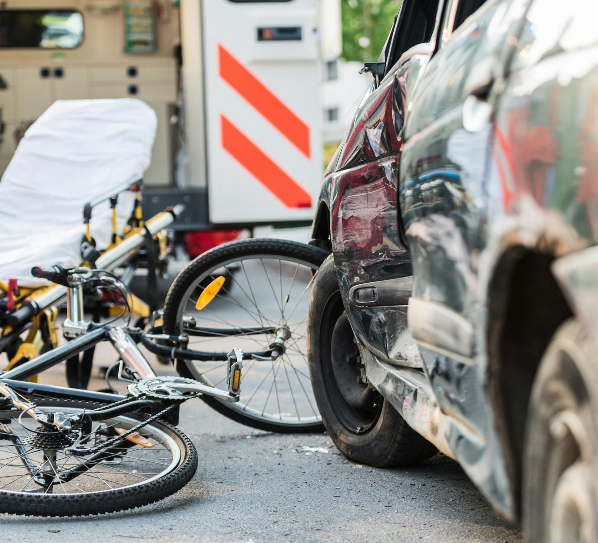 a bicycle is laying on the ground next to a badly damaged car with an ambulance in the background