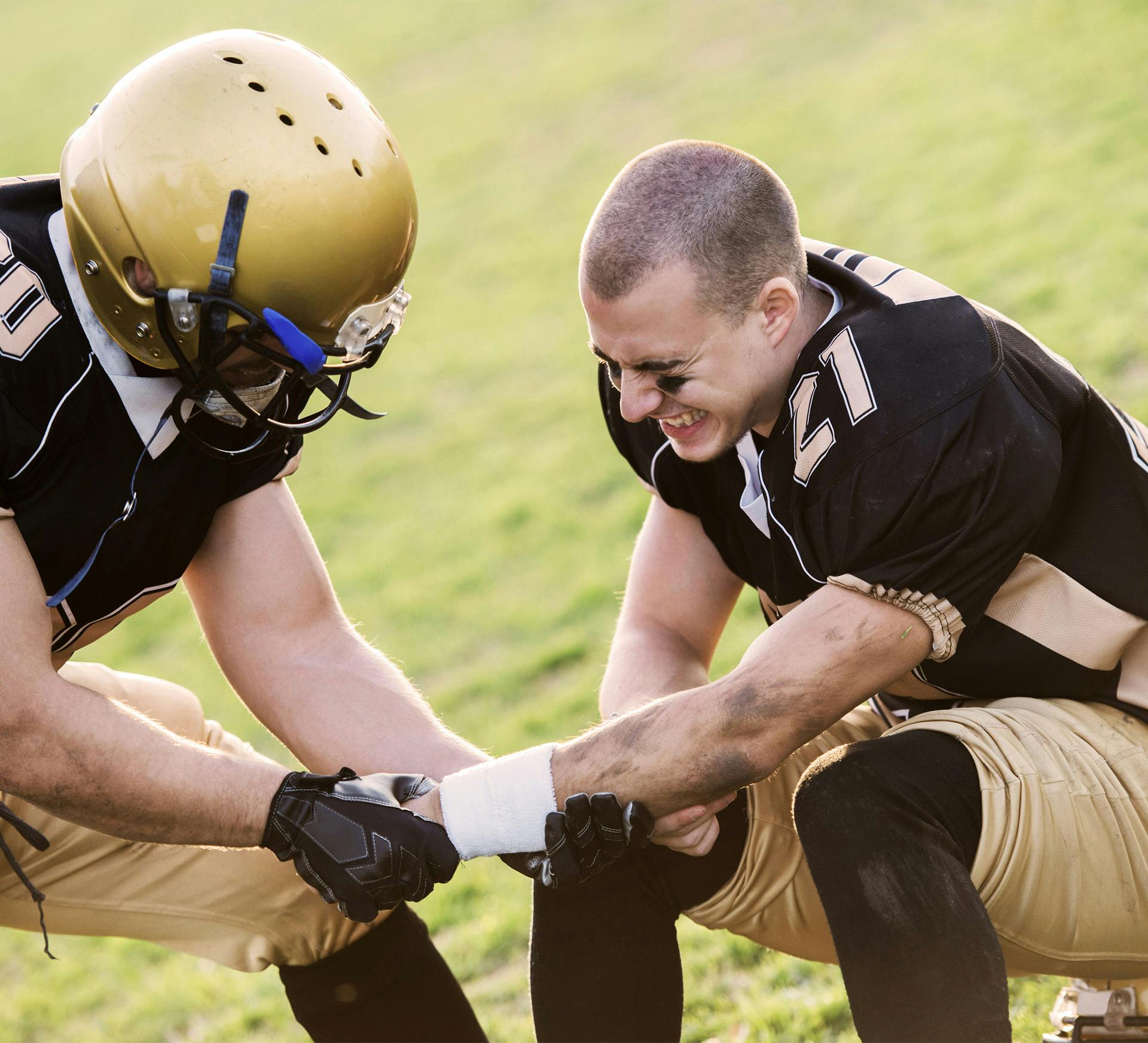 one football player looks in pain while other player helps straighten left arm