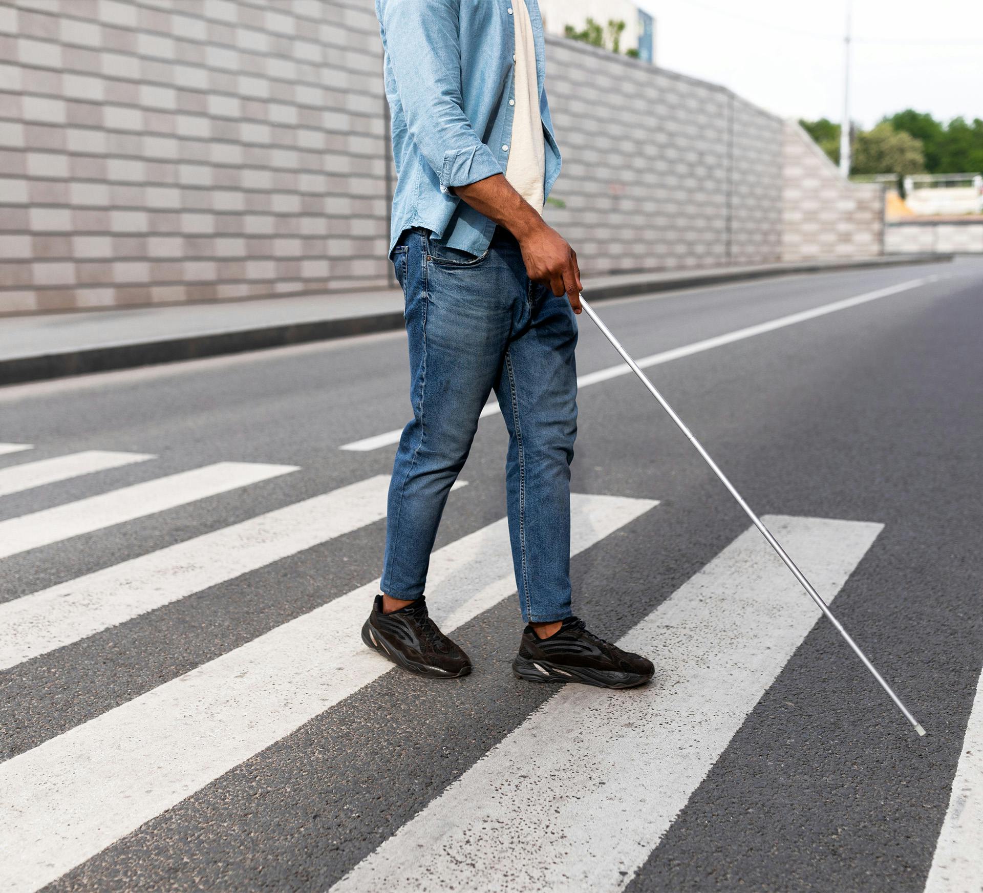 man with a blind person stick crossing a street on a crosswalk