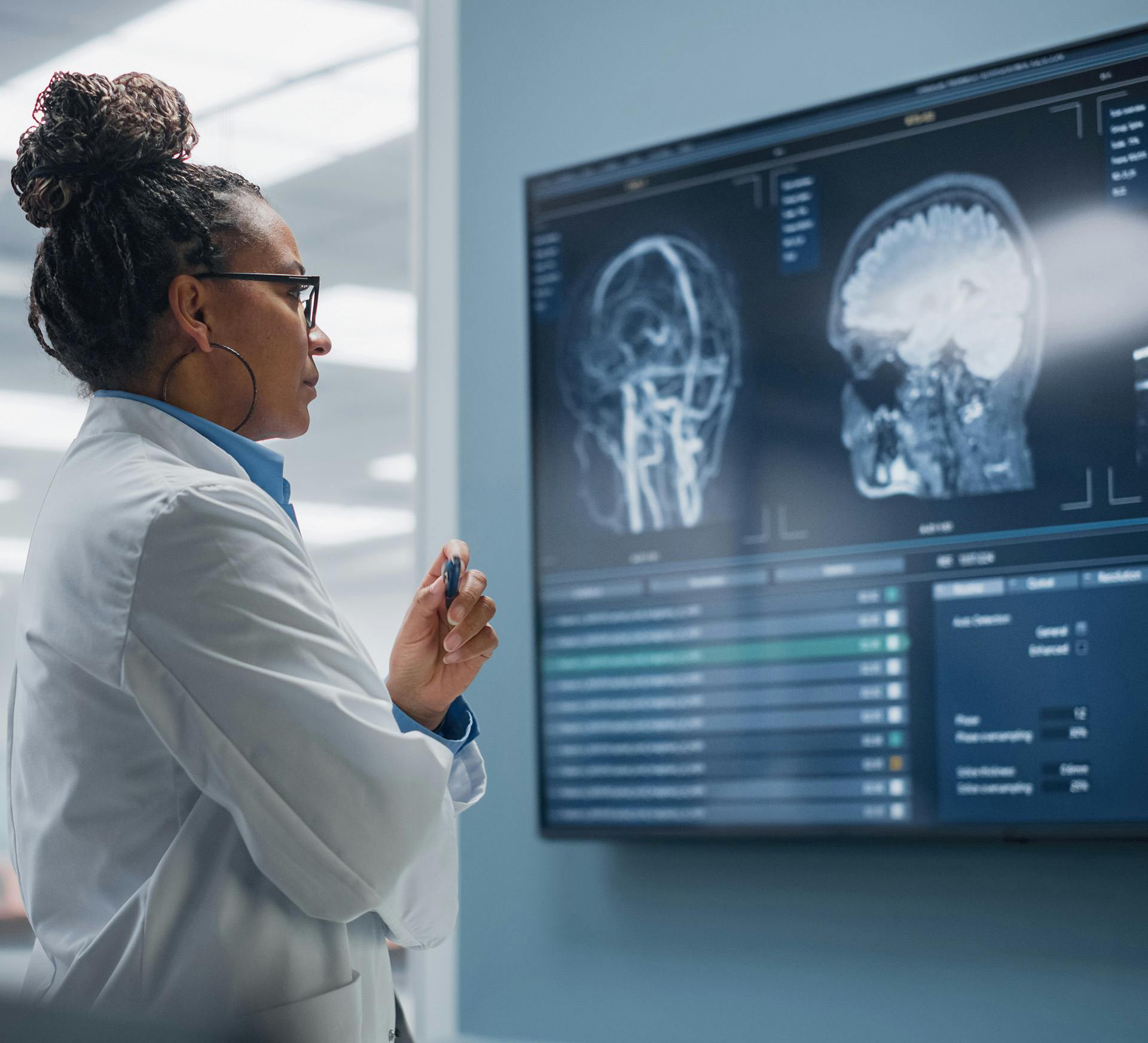 woman in lab coat looking at a computer screen with brain x-ray scans