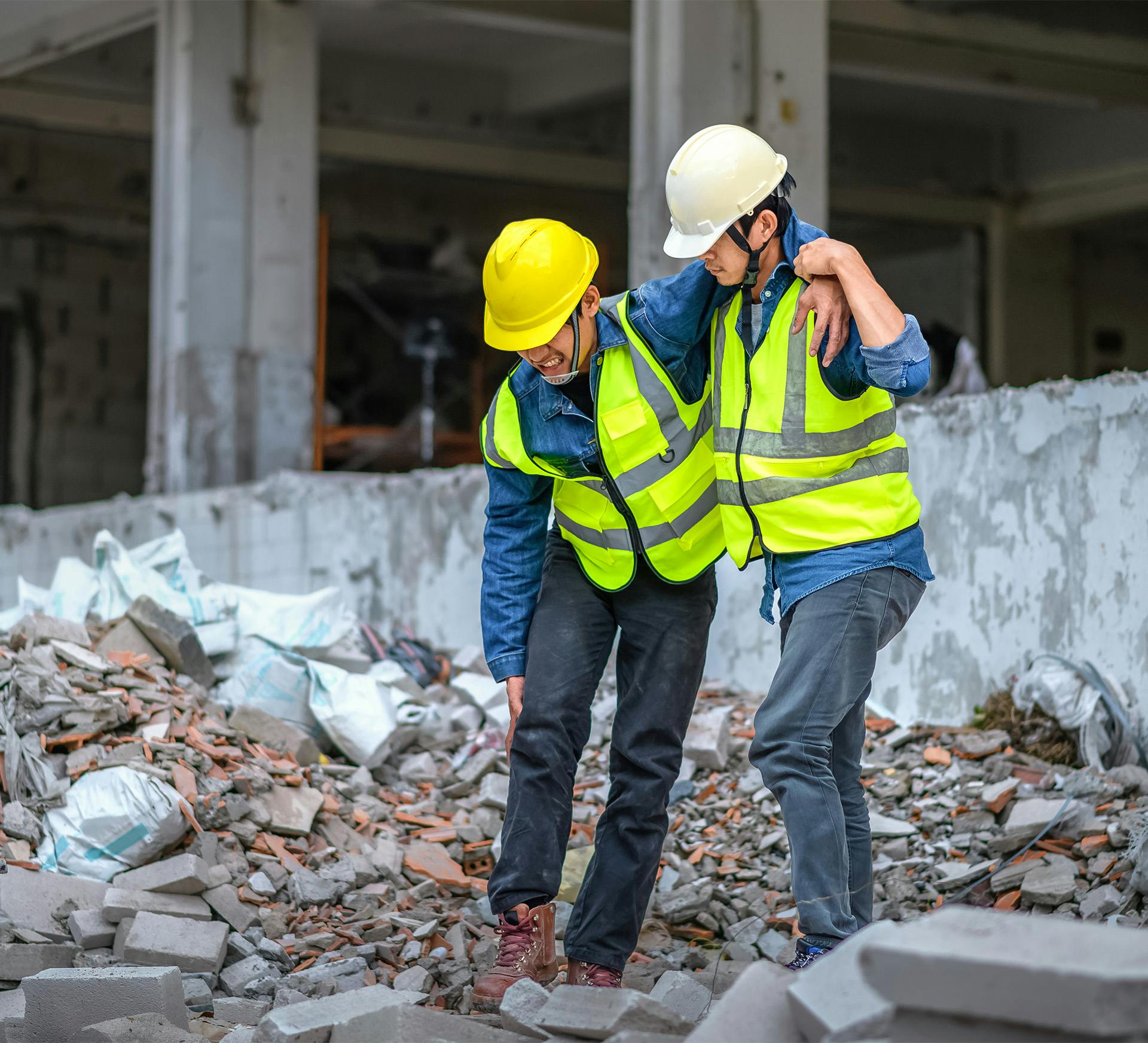 construction worker with broken leg being helped by co-worker across building rubble