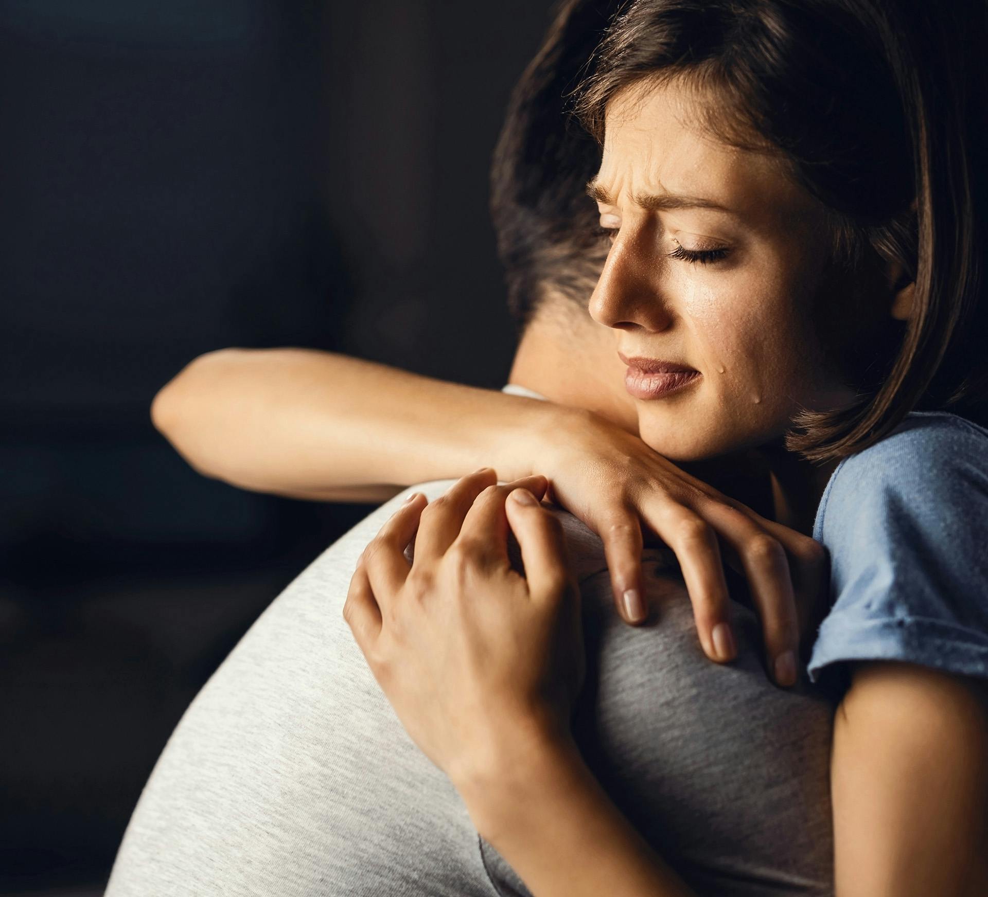 crying woman hugging a man in a white shirt with black background
