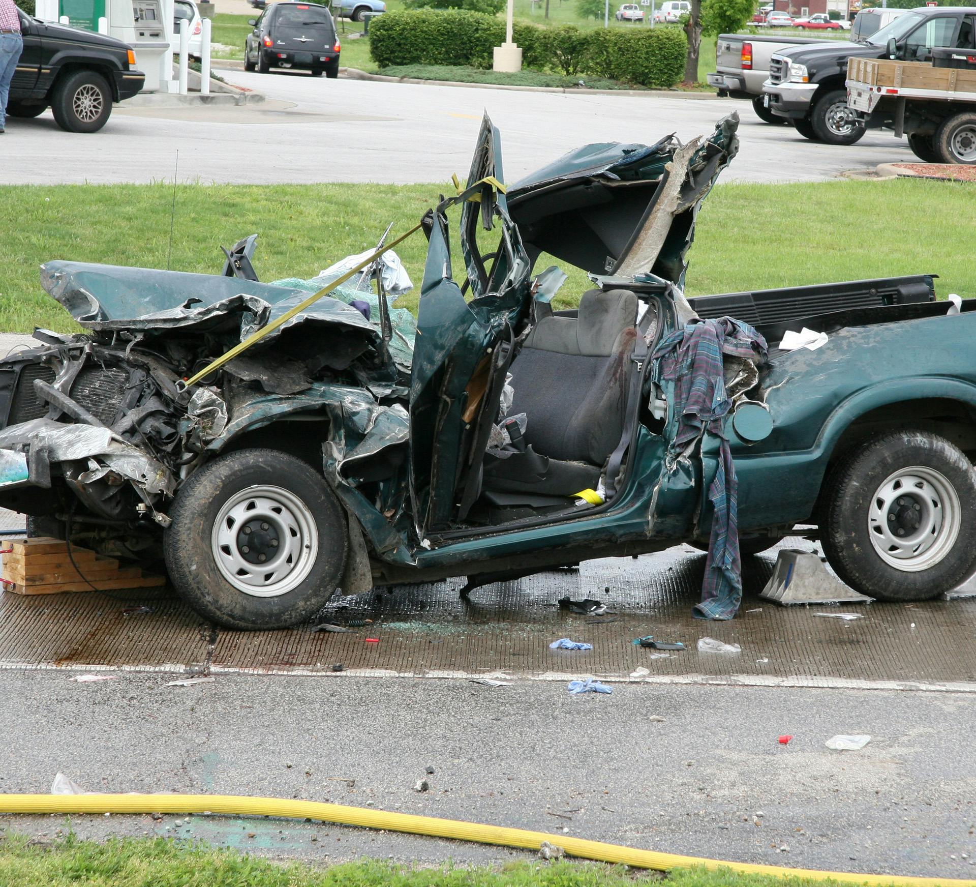 a green truck that has been badly wrecked and is on side of road