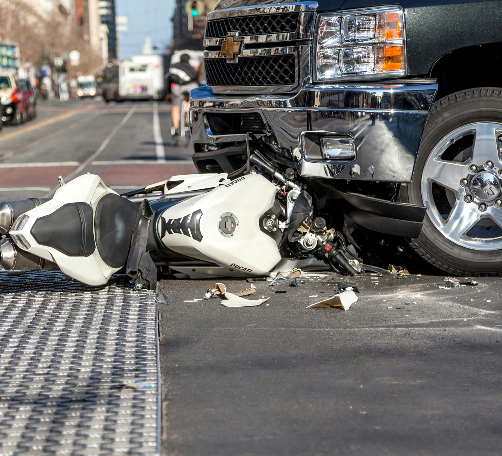 a smashed motorcycle underneath a pickup truck front carriage