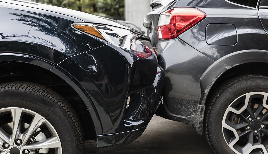 picture of black vehicle front bumper touching the back bumper of a grey vehicle
