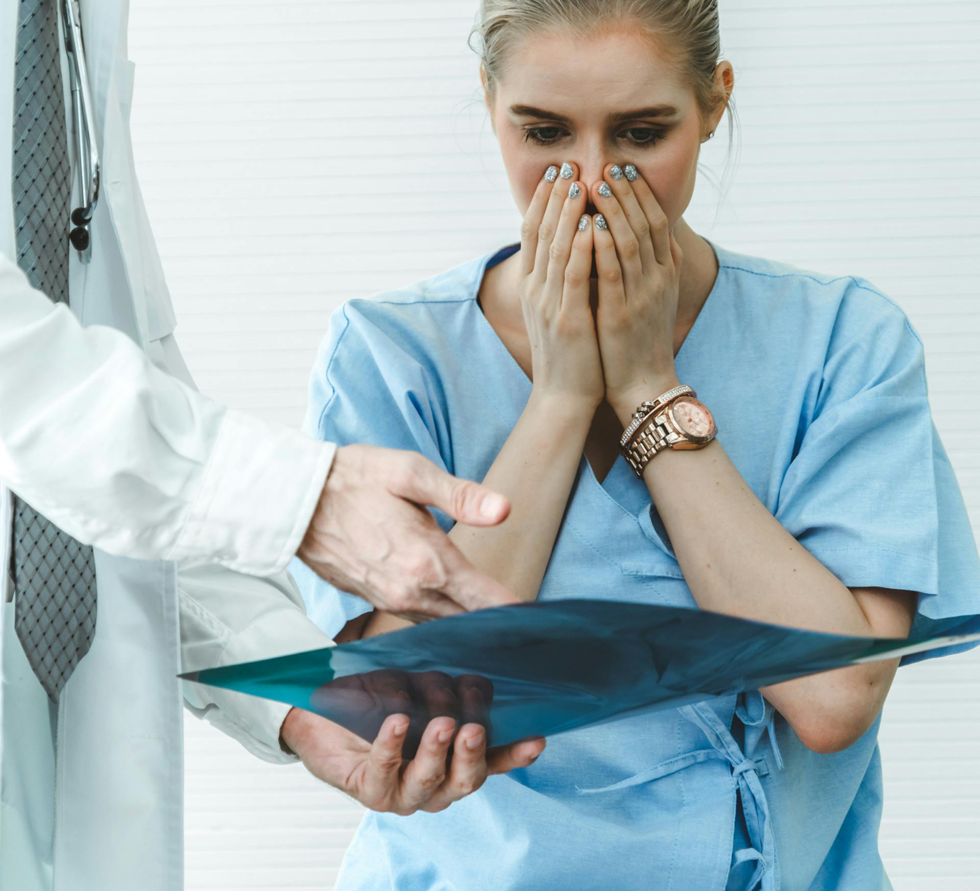 woman in scrubs covering her face with hands while looking at clipboard