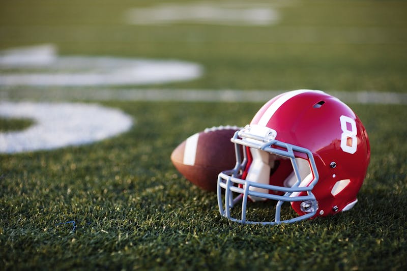 A red American football helmet and football on the football field