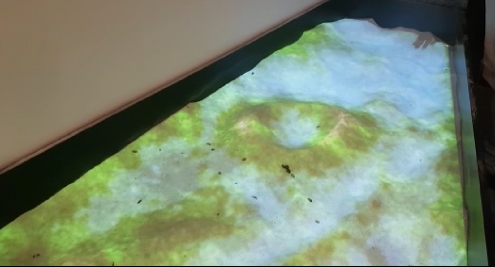 Sandbox surface with a sand crater and hills shown in projected green, brown and pale blue.