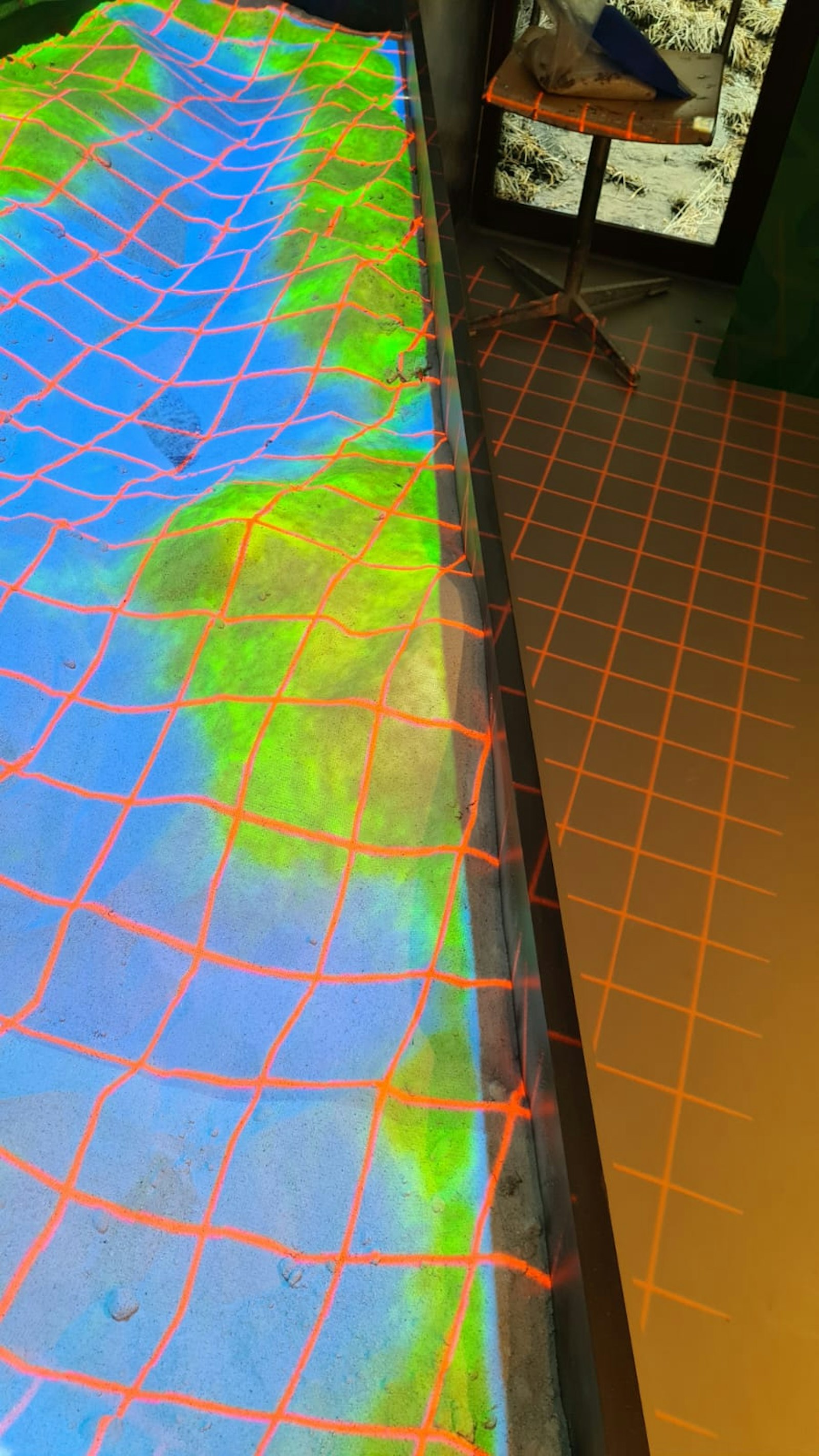 Calibration grid projected in orange lines over the sandbox and onto the floor beside it.
