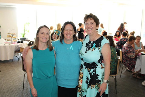 Three women wearing teal at a lunch event