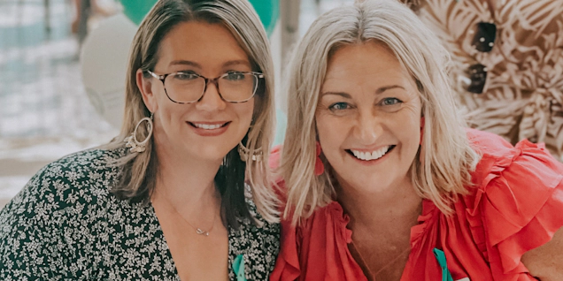 Two women seated at a table with teal balloons