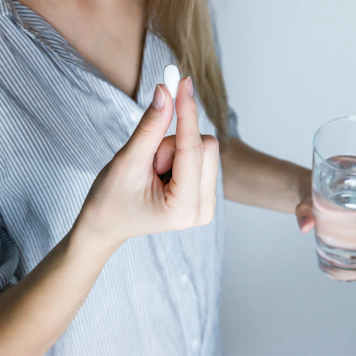 Woman holding pill and glass of water