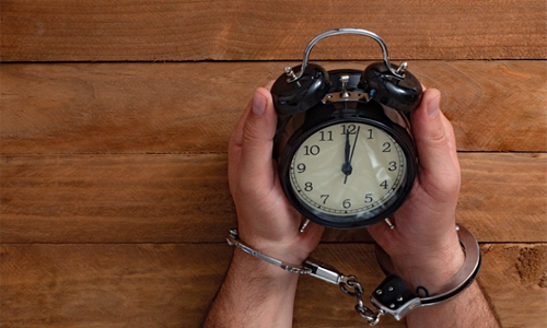 Man wearing handcuffs and holding an alarm clock