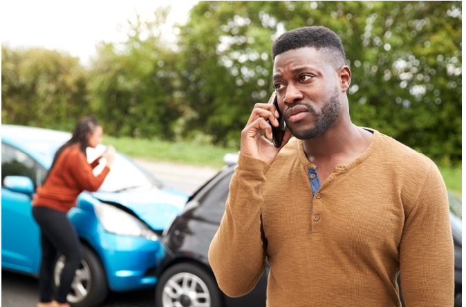 Man talking on his phone next to a car crash.