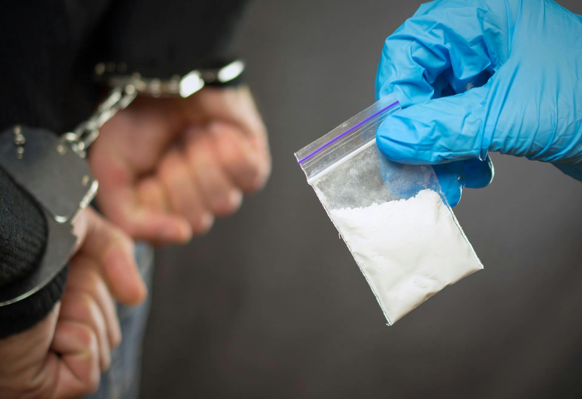Man in cuffs next to a baggie of white powder.