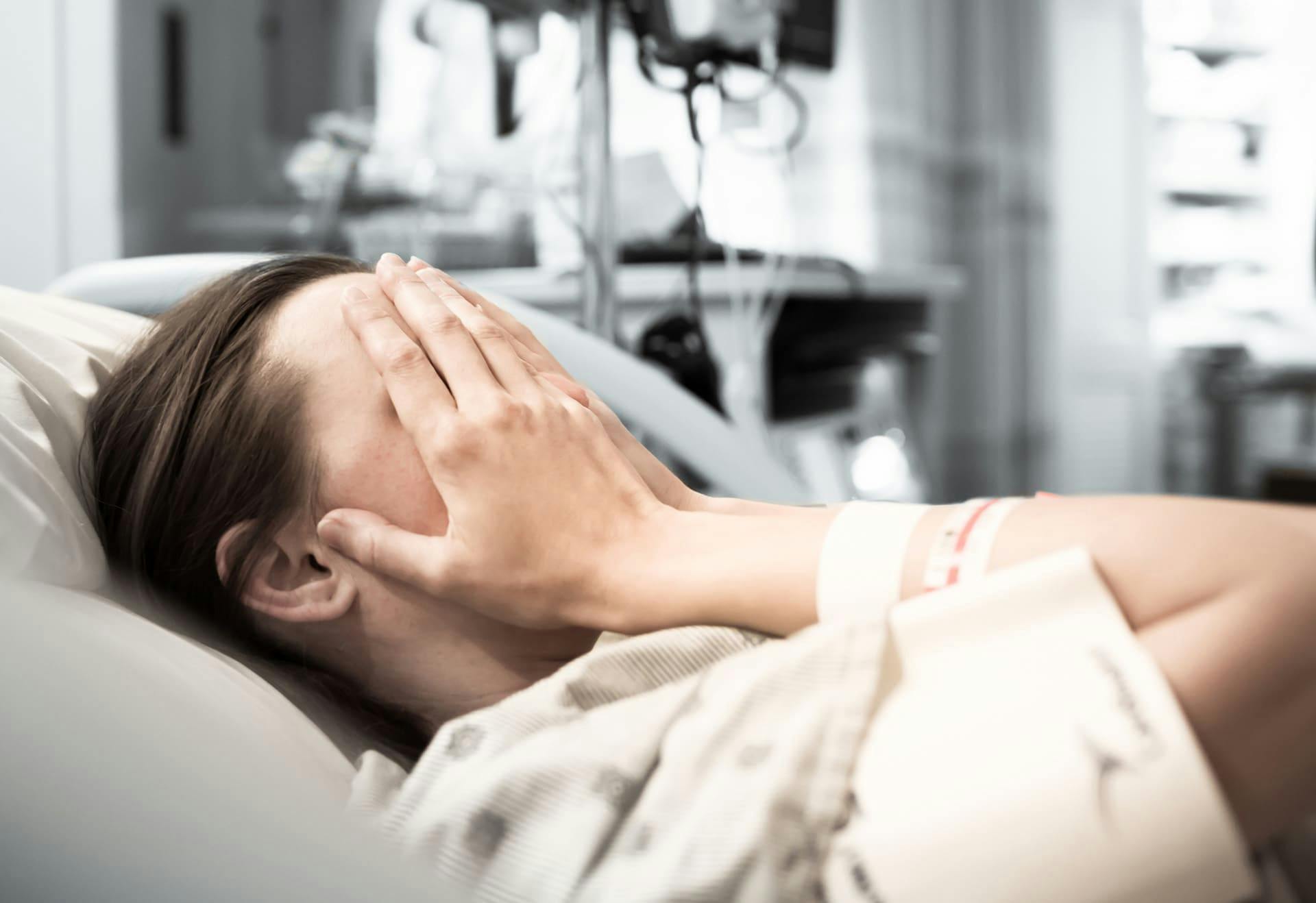 Person in hospital bed with hands over her face.