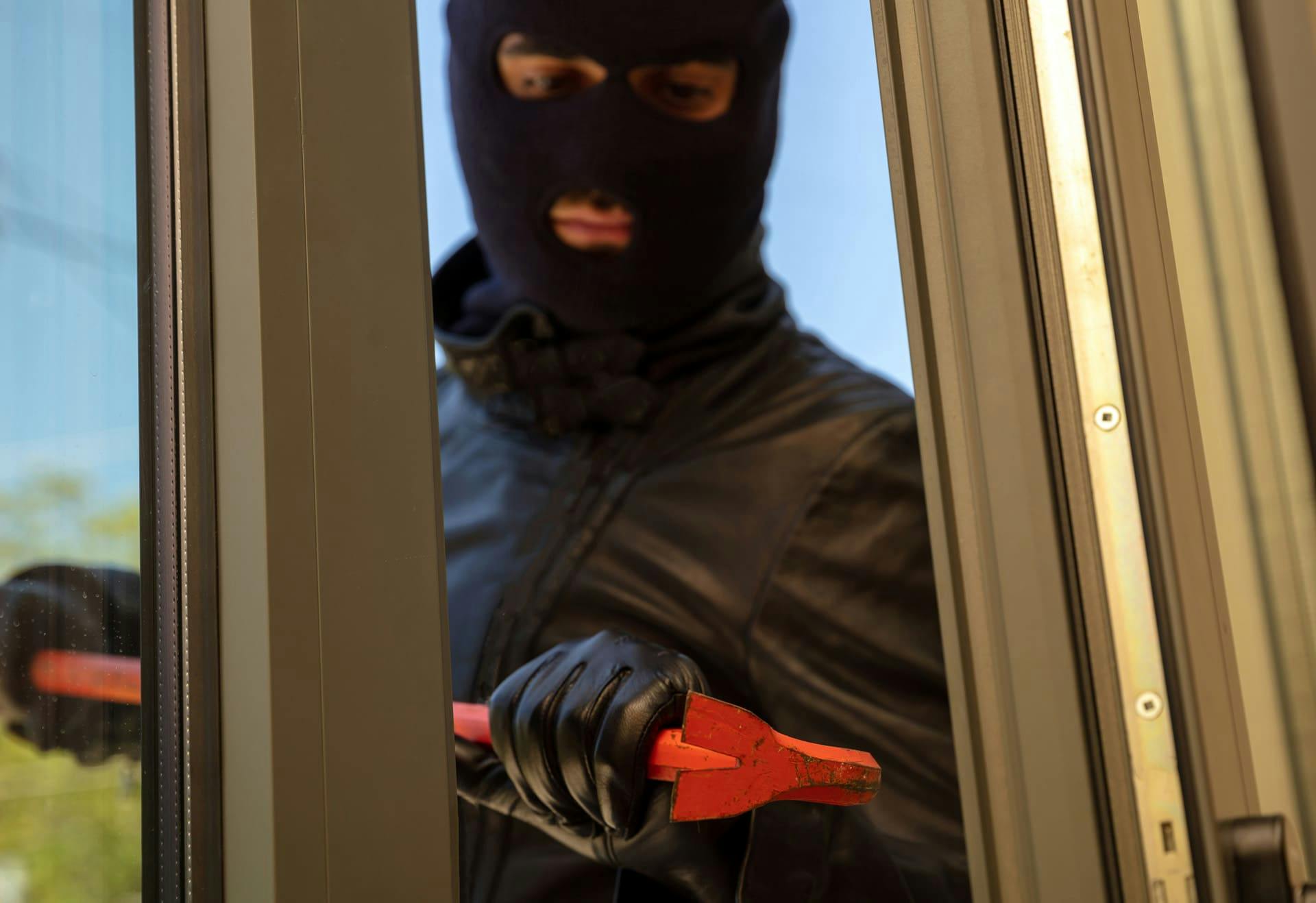 Masked man with a crowbar next to a door