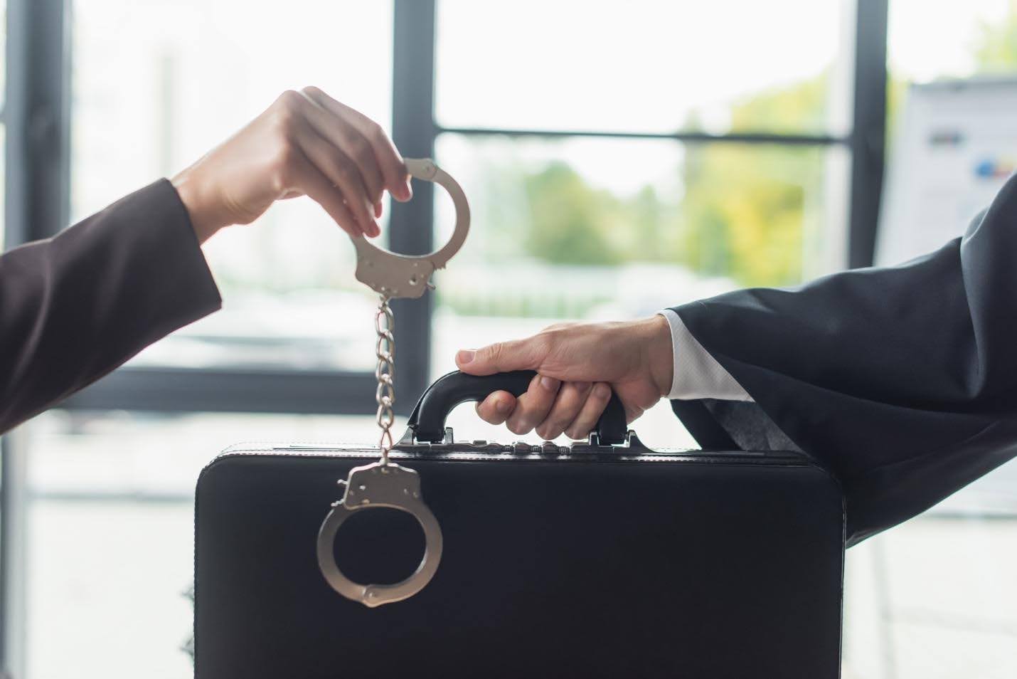 Person handing handcuffs to someone else holding a briefcase