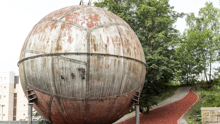 suuri ruostunut metallipallo on vehreän rinteen päällä