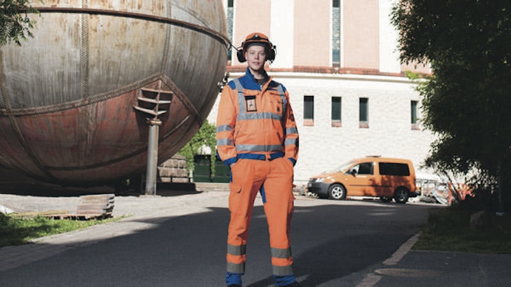 oranssissa turvapuvussa oleva mies seisoo suuren veneen edessä