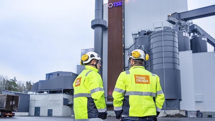 kaksi miestä keltatakkeissa seisomassa tehtaan edessä