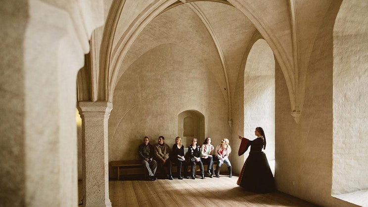 ryhmä ihmisiä istumassa penkeillä rakennuksessa