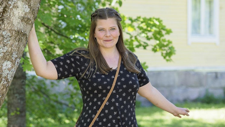 nainen seisoo puun vieressä pitelemässä kukkaroa