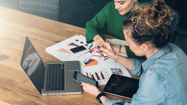 pari naista on pöydän ääressä kannettavien tietokoneiden kanssa