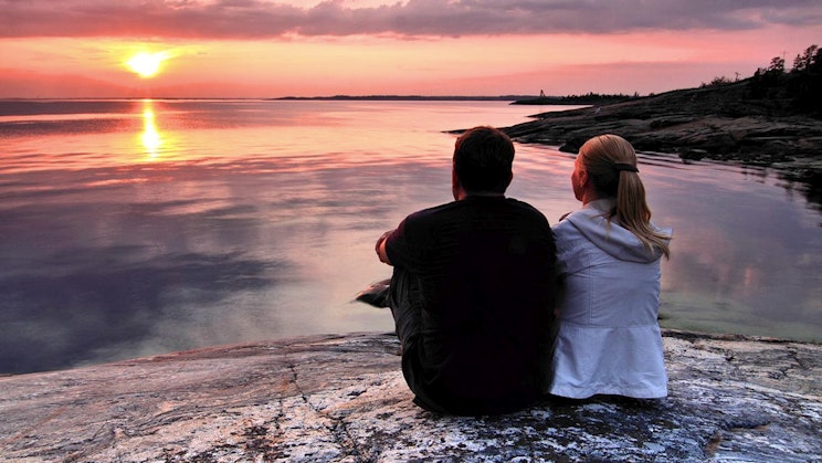 mies ja nainen istuvat kivellä katsomassa auringonlaskua