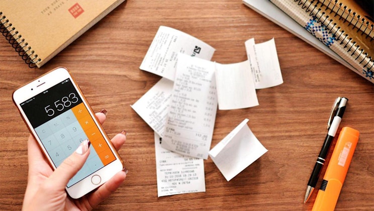 henkilö pitelee kännykkää paperikasan vieressä