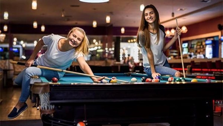 kaksi naista pelaa biljardia baarissa