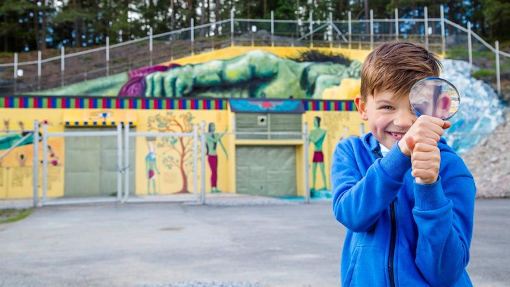 nuori poika pitelee suurennuslasia seinämaalauksen edessä