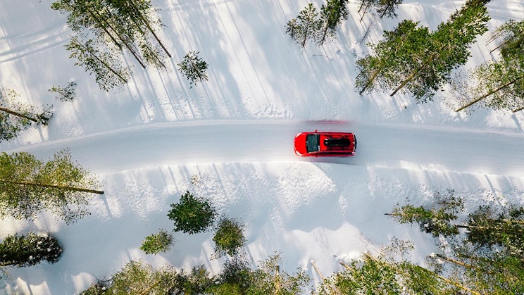 punainen auto ajaa lumisessa metsässä