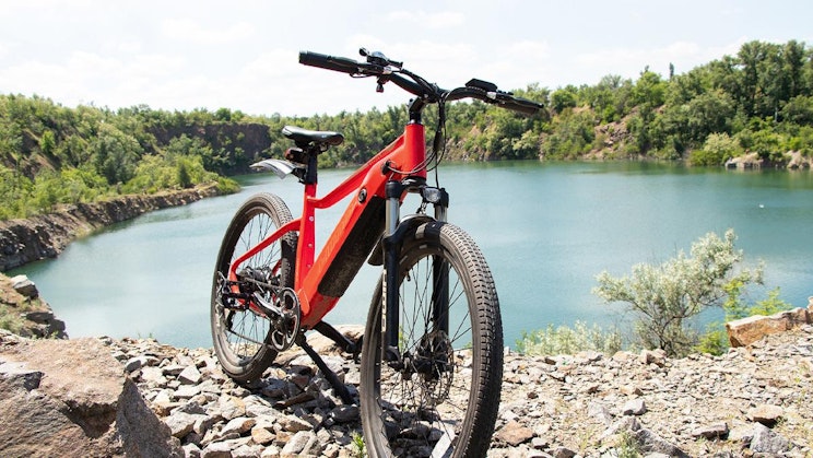punainen pyörä pysäköitynä kiviselle rinteelle järven viereen