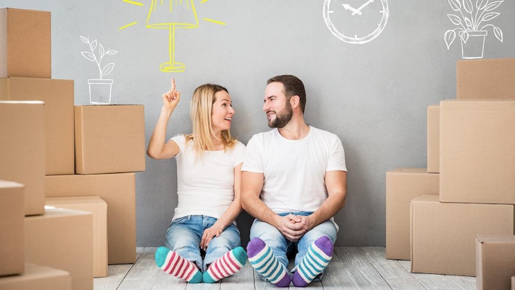 mies ja nainen istuvat lattialla pahvilaatikoiden ympäröimänä