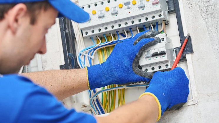 mies sinisissä käsineissä työskentelemässä sähköpaneelilla