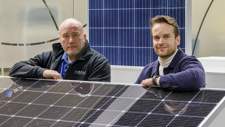 Kaksi ihmistä seisomassa ja nojaamassa aurinkopaneliin.