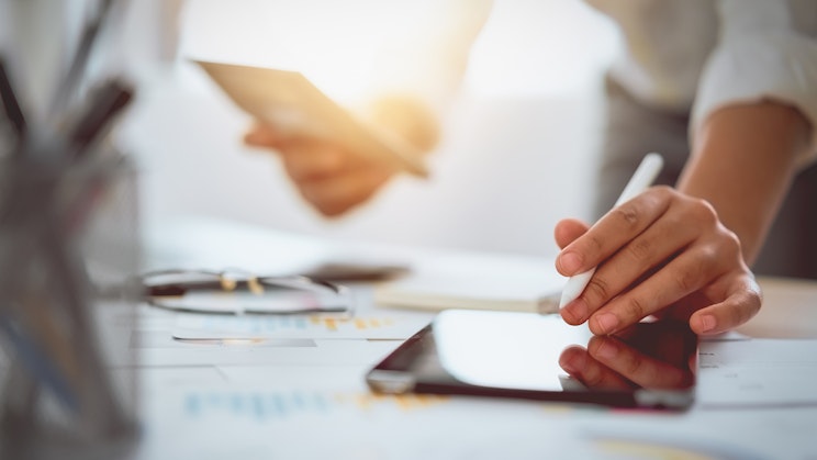 Henkilö on pöydän ääressä ja käyttää tablettia kynän kanssa.