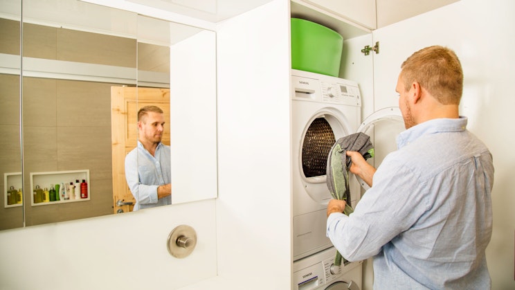 Miesoletettu laittamassa pyykkiä pyykkikoneeseen.